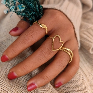 Close-up of gold hollow heart and wavy stackable rings worn with a knitted sweater