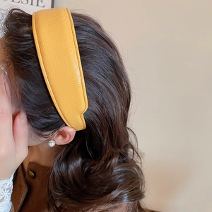 Detail view of a bright yellow pleated leather headband on hair with pearl accessory
