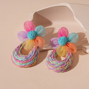Detail of handmade woven raffia flower earrings with colorful mesh fabric on a stone base