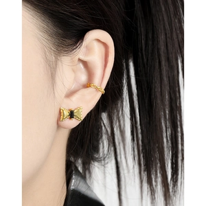 Golden bow stud earrings with black gemstone and chain cuff shown on model ear