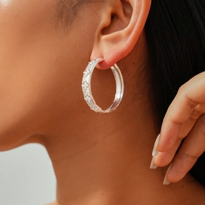 Macro detail of silver hoop earrings with zircon floral accents on a model's ear