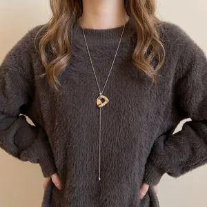 Minimalistische goldene lange Halskette mit unregelmäßigem Anhänger auf braunem Pullover