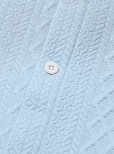 Close-up of light blue knitted shirt fabric with geometric texture and white button