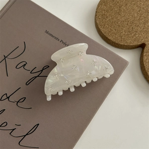 Pinza per capelli in resina bianco perlato con strass a stella su un libro