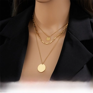 Detail of a layered gold necklace featuring three chains and circular pendants on a black suit