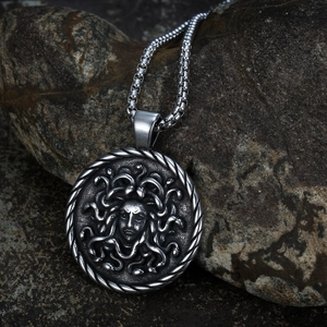 Vintage Medusa relief pendant necklace in antique silver finish on a dark rock background
