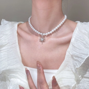 Close-up of pearl necklace featuring a silver star pendant worn on the neck