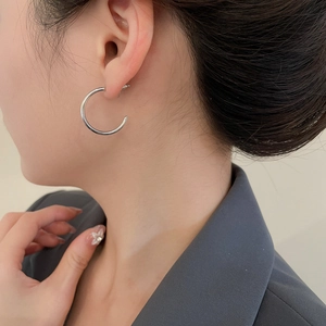 Silver C-shaped metallic hoop earrings worn by a model in a modern professional look