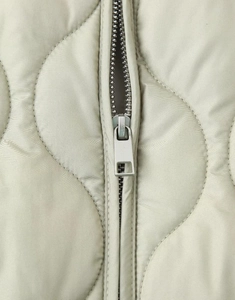 Detail of light beige onion quilted jacket showing wavy stitching and silver metal zipper