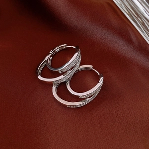 Macro shot of silver double-layered hoop earrings with zircons on dark red silk