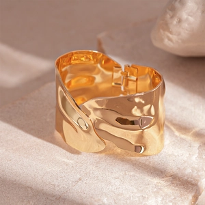 Macro detail of a wide gold metal hinged bracelet with unique hammered lava texture