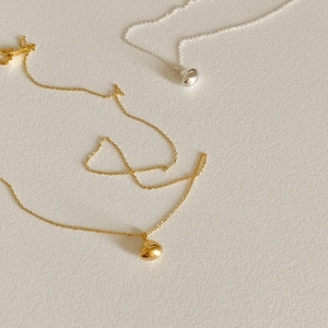 Close-up of minimalist gold and silver bean pendants on delicate metal chain necklaces