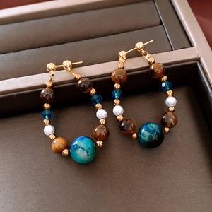 Détail de boucles d'oreilles en perles et oeil de tigre dans un coffret en velours brun