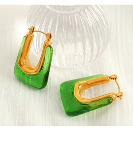 Macro shot of U-shaped gold earrings with green resin inlays on textured fabric