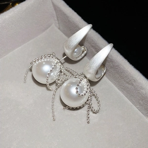 Close-up of pearl earrings with silver beaded tassels on a grey velvet display tray