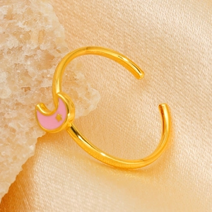 Detail of gold titanium ring with pink moon and star charms on silk background