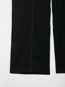 Detail of black straight trousers featuring high-contrast yellow decorative topstitching