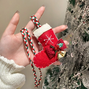 Close-up of handmade Christmas stocking pendant with bells and bow on a woven cord