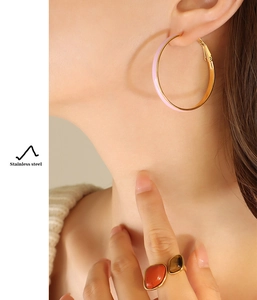 Close-up of gold stainless steel hoop earrings with pink enamel on a female model