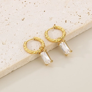 Détail de boucles d'oreilles créoles dorées texturées avec pendentif zircon rectangulaire