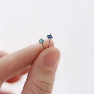 Macro view of tiny silver-tone stud earrings featuring bright light and dark blue stones