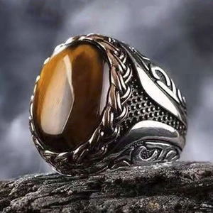 Macro shot of men's vintage copper ring with oval tiger eye stone on black rock