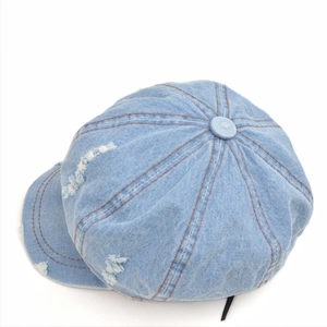 Detailed view of the distressed light blue denim fabric and brown stitching on the cap