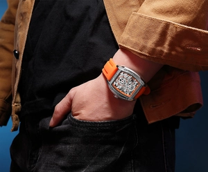 Macro view of tonneau mechanical watch featuring orange silicone strap and hollow dial