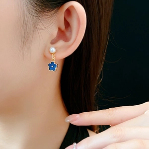 Close-up of blue flower drop earrings with pearls on a model, featuring gold trim detail