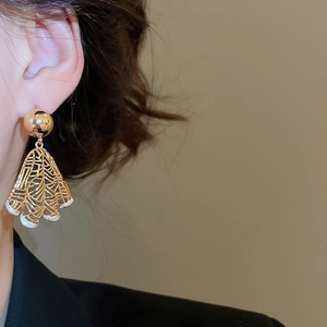 Close-up of a model wearing golden fan-shaped hollow earrings with white enamel details