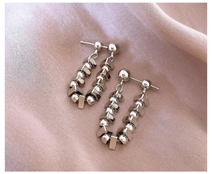 Detailed view of silver U-shaped earrings with metallic beads on pink satin fabric