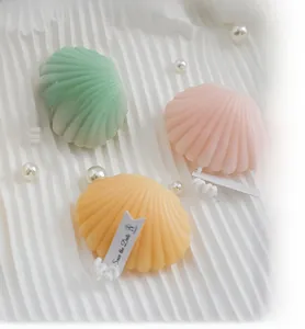 Close-up of shell-shaped scented candles in pastel colors on white fabric with pearls