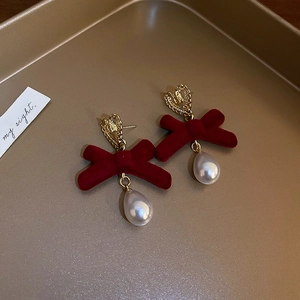 Macro detail of red velvet bow earrings with gold heart studs and pearl drops