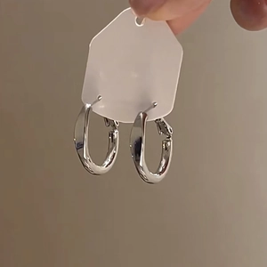 Detail of silver C-shaped hoop earrings on white tag held by hand with metallic finish