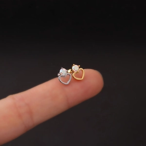 Macro shot of silver and gold heart stud earrings with rainbow zircon on a fingertip