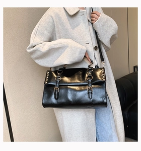 Detail of black faux oil wax leather satchel bag featuring gold buckles and rivet accents