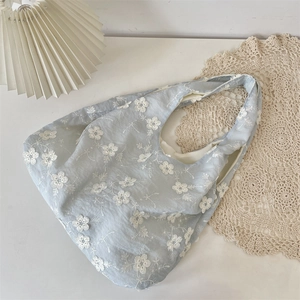 Top view of a light blue embroidered floral canvas tote bag on a cozy home setting
