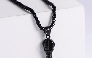 Detail of a black box chain necklace with a spherical crown pendant on white stone