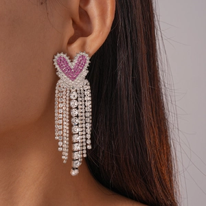 Détail des boucles d'oreilles cœur en strass roses avec de longs pompons argentés