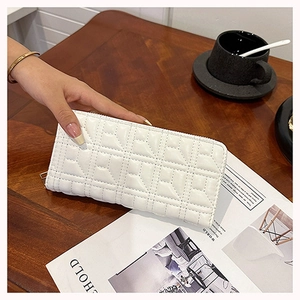 Detailed view of a white quilted long wallet on a wooden table with lifestyle accessories