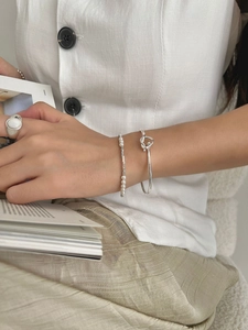 Detail of silver knot bangle, pearl bracelet and white stone ring on model holding a book