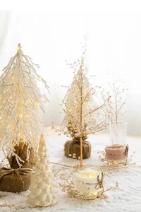 Mini white flocked Christmas trees with gold LED ornaments and candle on wooden table