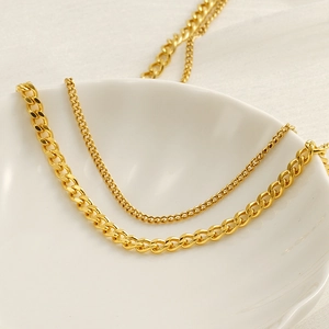 Detailed view of layered gold cuban and thin cable chain necklaces on a white ceramic bowl