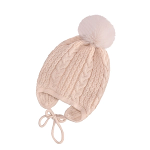 Detail of baby cable knit hat with large pompom and earflaps in cream color