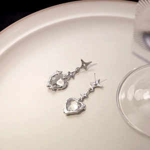 Macro detail of long silver drop earrings featuring heart-shaped zircon on a ceramic tray