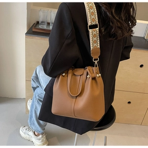 Brown litchi leather bucket bag featuring woven strap and gold hardware on model