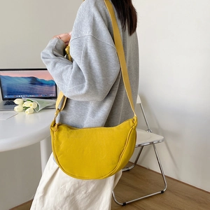 Yellow nylon dumpling crossbody bag worn by a model in a minimalist bright indoor setting