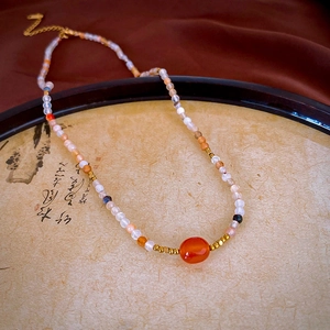 Artistic close-up of beaded necklace with orange agate bead on a vintage wooden tray