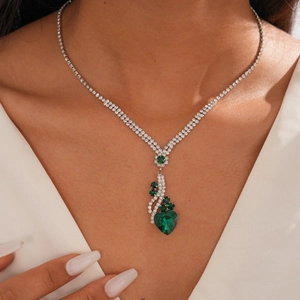 Gros plan d'un collier argenté avec pendentif cœur vert porté par un mannequin en col V