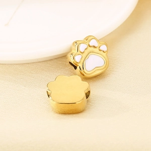 Detail of golden stainless steel paw pendants with white enamel filling on a ceramic tray